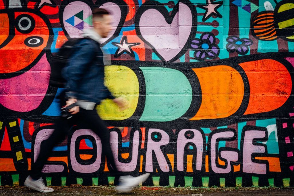 Man walking past wall with courage written on it